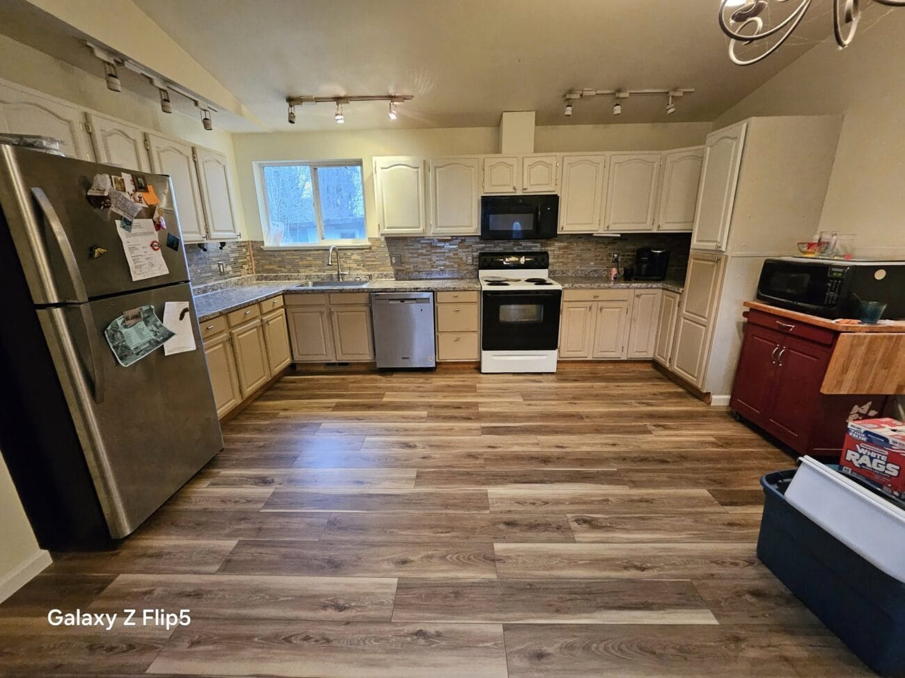 A spacious kitchen, perfect for any home renovation project, features wooden flooring, light cabinets, and a range of appliances including a fridge, stove, dishwasher, and microwave. A small island and a trash bin complete the functional charm of this culinary space.